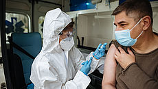 Ein Mann mit medizinischer Maske wird in einem Rettungswagen geimpft.
