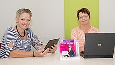 Zwei Frauen sitzen mit Tablet und Laptop an einem Tisch