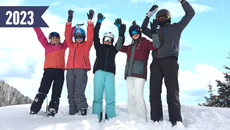 5 Personen in Skianzug stehen im Schnee und winken in die Kamera