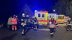 Vier Rettungsfahrzeuge und mehrere Rettungskräfte befinden sich während einer Übung vor einem Haus. Es ist Nacht.