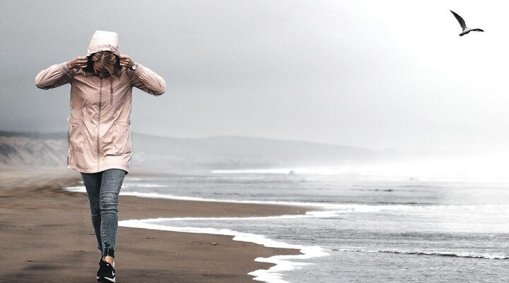 Frau spaziert bei stürmischen Wetter an der Küste