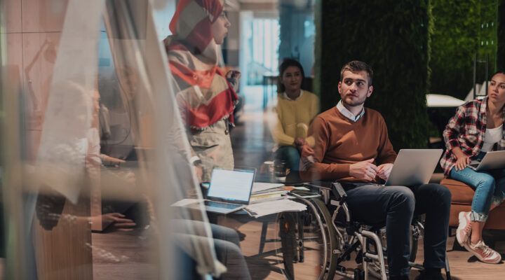 Eine Geschäftsfrau präsentiert ein Projekt vor einem jungen, vielfältigen Team von Menschen in einem modernen Büro