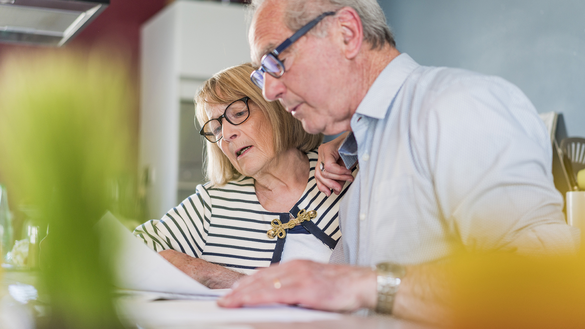 Älteres Paar sitzt gemeinsam am Tisch und schaut konzentriert auf ein Dokument, das sie zusammen durchgehen.