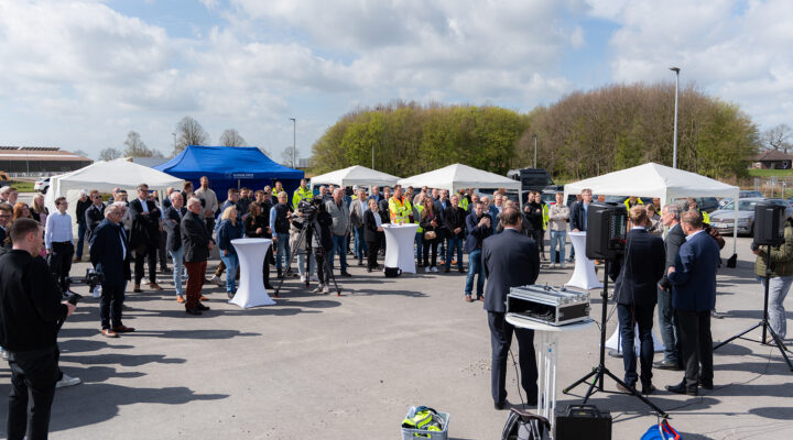 Große Gruppe von Menschen bei einer Outdoor-Veranstaltung mit Zelten und Stehtischen, während vorne mehrere Personen eine Ansprache halten.