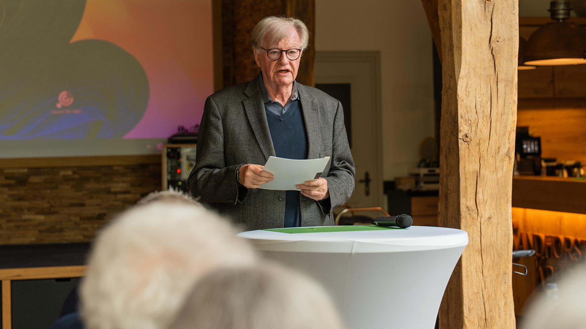 Das Bild zeigt Hans Michaelis während seiner Ansprache bei der Veranstaltung. Er steht an einem Stehtisch mit Unterlagen in der Hand und spricht vor den Gästen. Die Aufnahme vermittelt eine ruhige und konzentrierte Atmosphäre, passend zum feierlichen Charakter der Zusammenkunft.