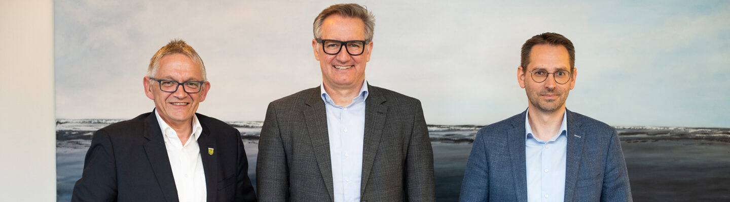Geschäftsführer der Landkreis Aurich Beteiligungs gGmbH Michael Hohlfeld zusammen mit Landrat Olaf Meinen (links) und Kreisrat Sebastian Smolinski (rechts). Im Hintergrund sieht man ein maritimes Gemälde von der Nordsee.
