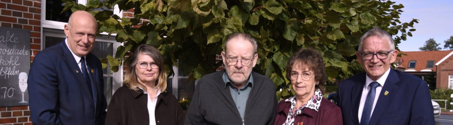 Gruppe von fünf Personen steht vor einem Gebäude; in der Mitte halten Frau Käthe Wiemers sowie Hinrich Wiemers eine Urkunde.