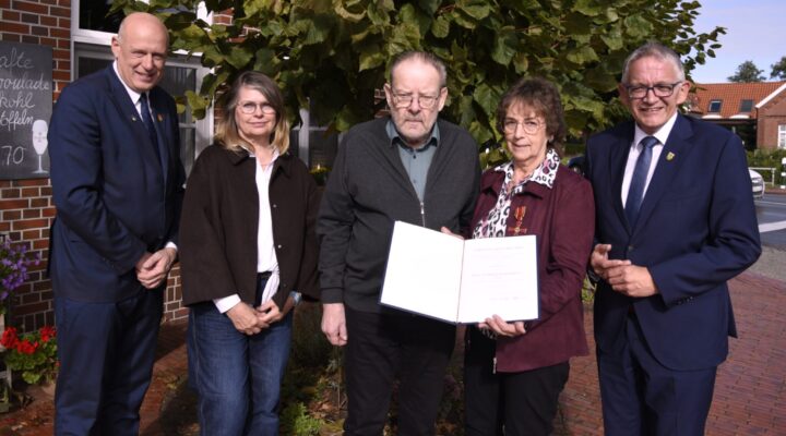 Gruppe von fünf Personen steht vor einem Gebäude; in der Mitte halten Frau Käthe Wiemers sowie Hinrich Wiemers eine Urkunde.